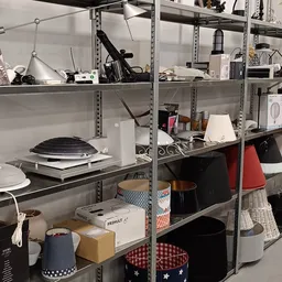 Metalen stellingen met diverse huishoudelijke artikelen en elektronica, waaronder pannen, lampen, dozen en keukenspullen