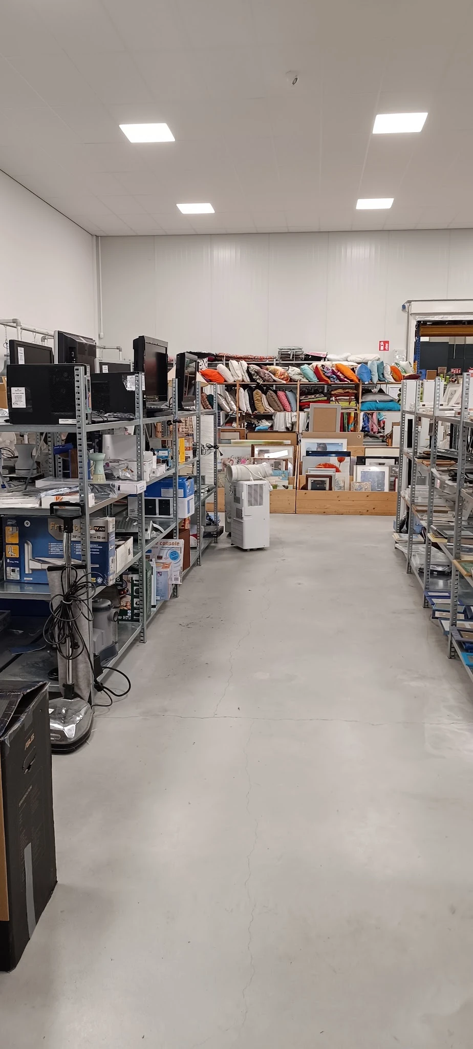 Winkelvloer met stellingen vol elektronische apparaten, boeken, kleding en diverse goederen in een kringloopwinkel
