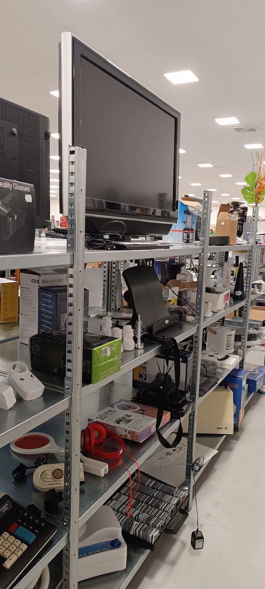 Metalen stellingen met diverse elektronische apparatuur en dozen in een kringloopwinkel