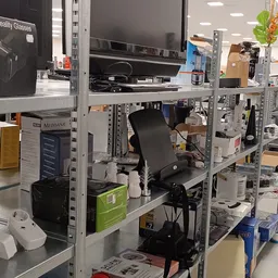 Metalen stellingen met diverse elektronische apparatuur en dozen in een kringloopwinkel