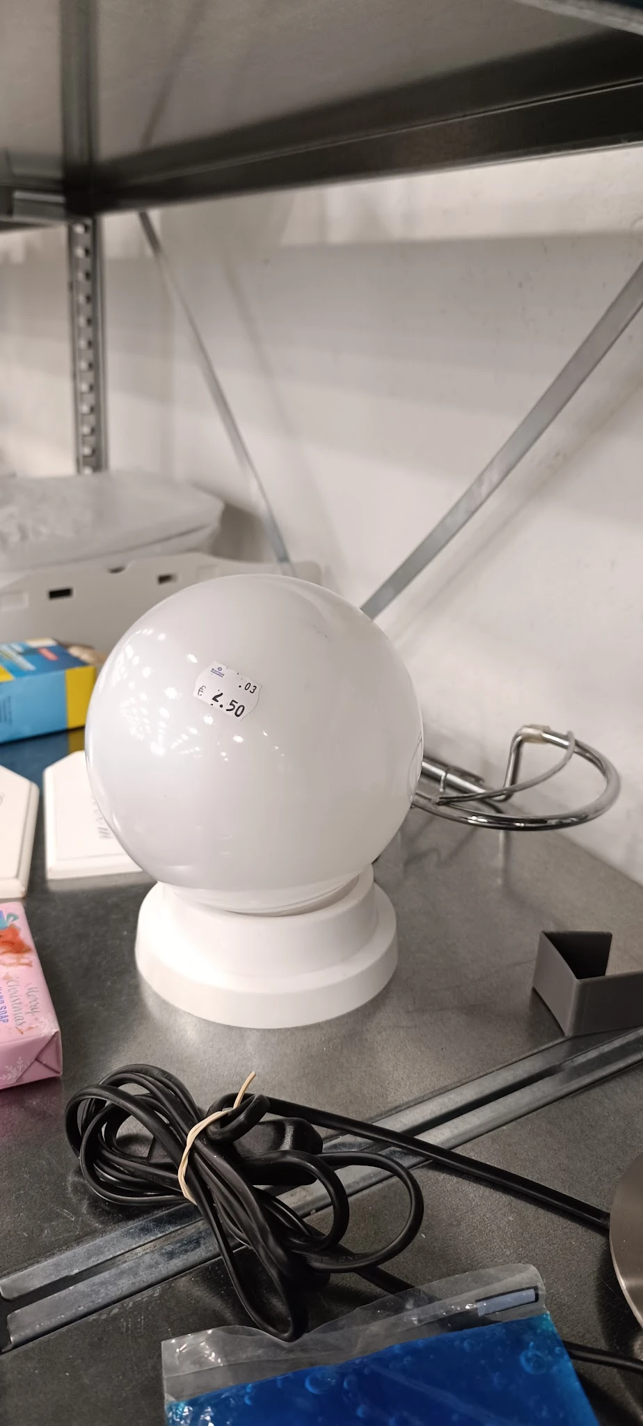 Witte bolvormige lamp met prijssticker op voet, staande op witte ondergrond