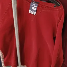 Close-up van een rood sweatshirt met label 2Switch, hangend aan een rek