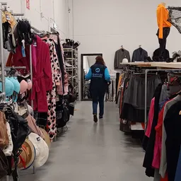 Winkelvloer van kringloopwinkel met rekken vol tweedehands kleding in verschillende kleuren, klant loopt door het gang