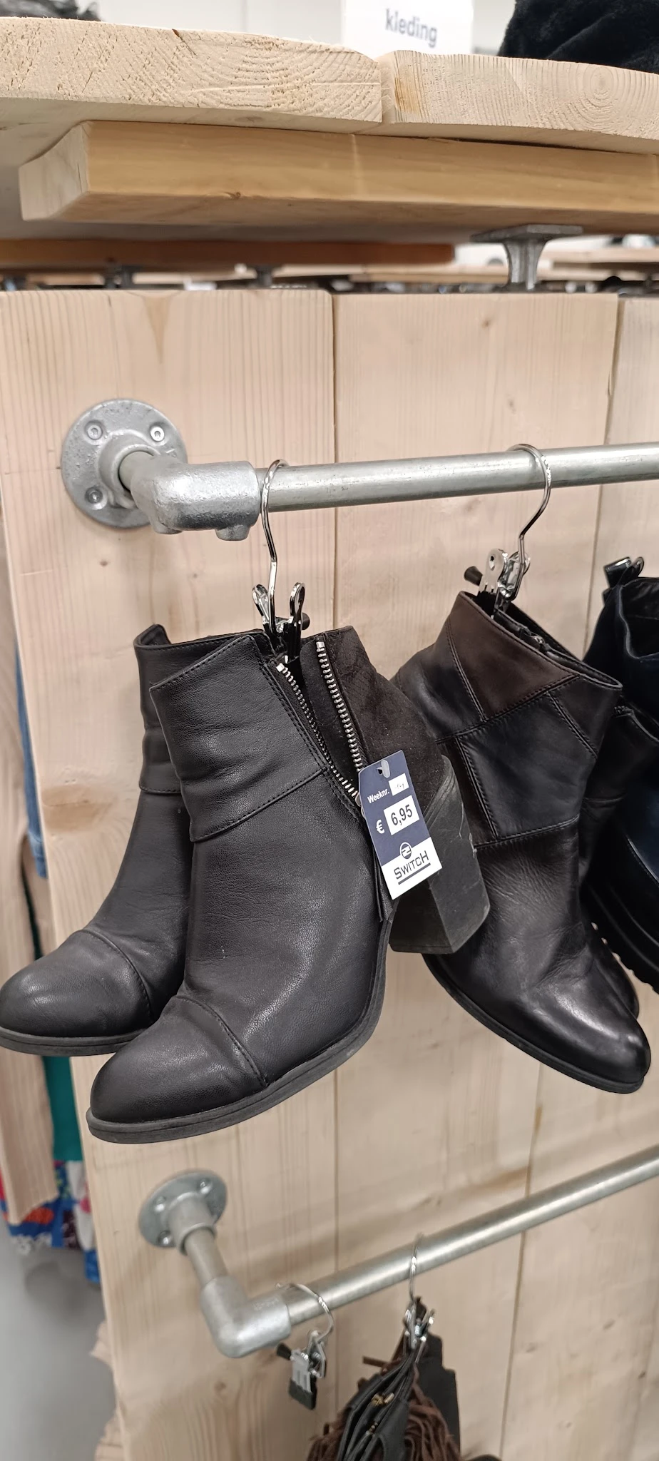 Zwarte leren dameslaarzen met rits opgehangen aan kledinghanger met prijskaartje