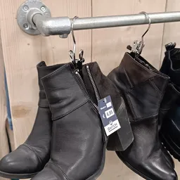 Zwarte leren dameslaarzen met rits opgehangen aan kledinghanger met prijskaartje