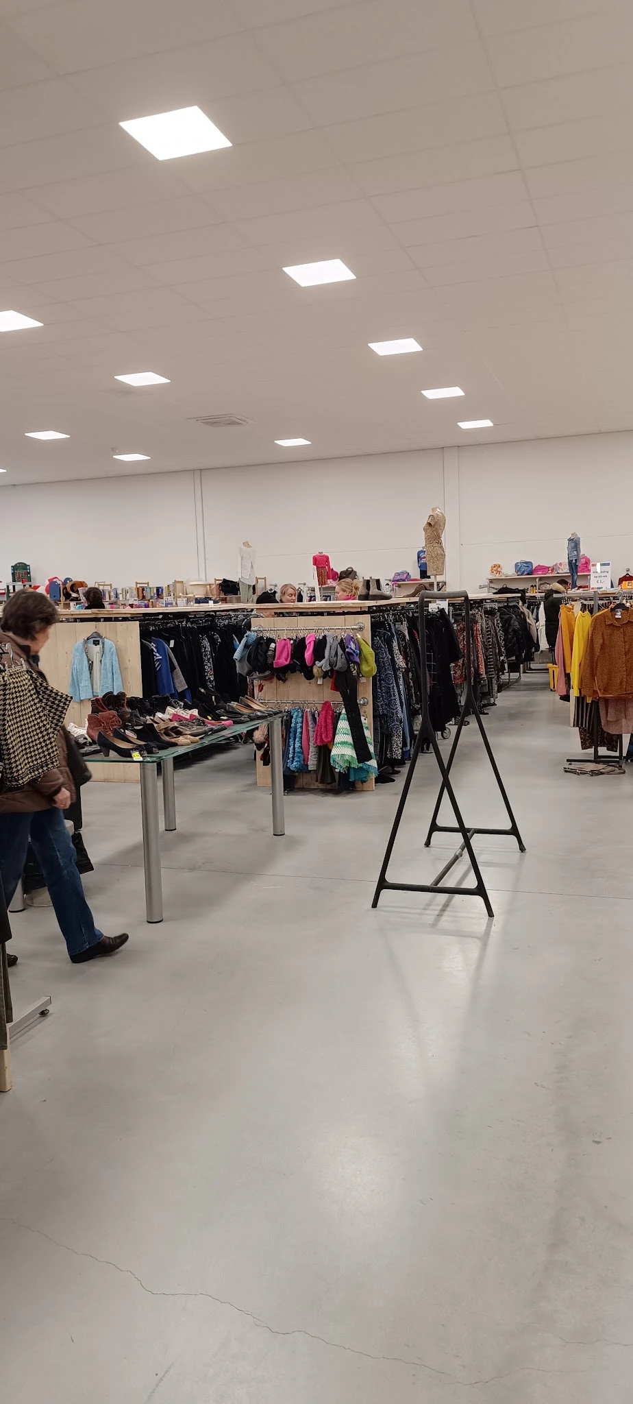 Winkelinterieur met kledingrekken, tafels met schoenen en getoonde kleding in verschillende kleuren