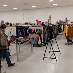 Winkelinterieur met kledingrekken, tafels met schoenen en getoonde kleding in verschillende kleuren