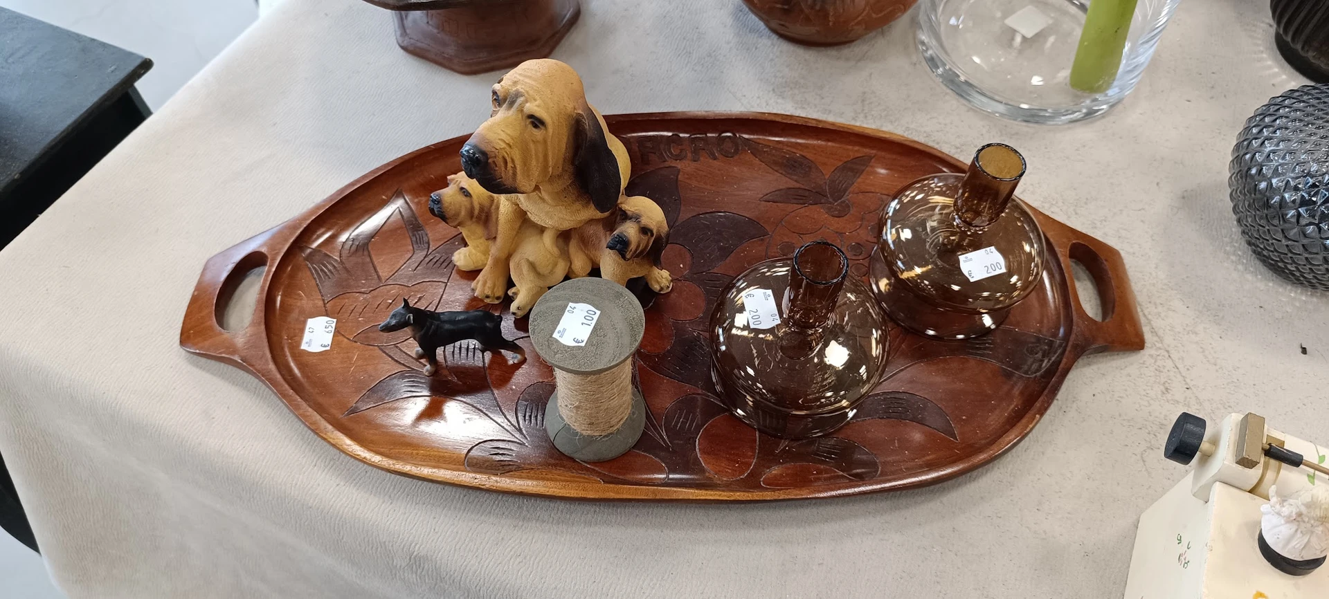 Houten dienblad met decoratieve items: gele hondenbeeldje, bruine glazen flesjes, klein potje en vis-ornament.
