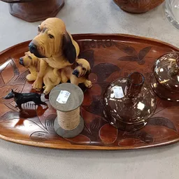 Houten dienblad met decoratieve items: gele hondenbeeldje, bruine glazen flesjes, klein potje en vis-ornament.