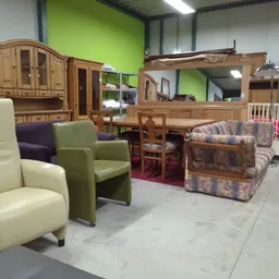 Kringloopwinkelruimte met diverse meubels: stoelen, kasten, beds en een antieke koffer op rood tapijt