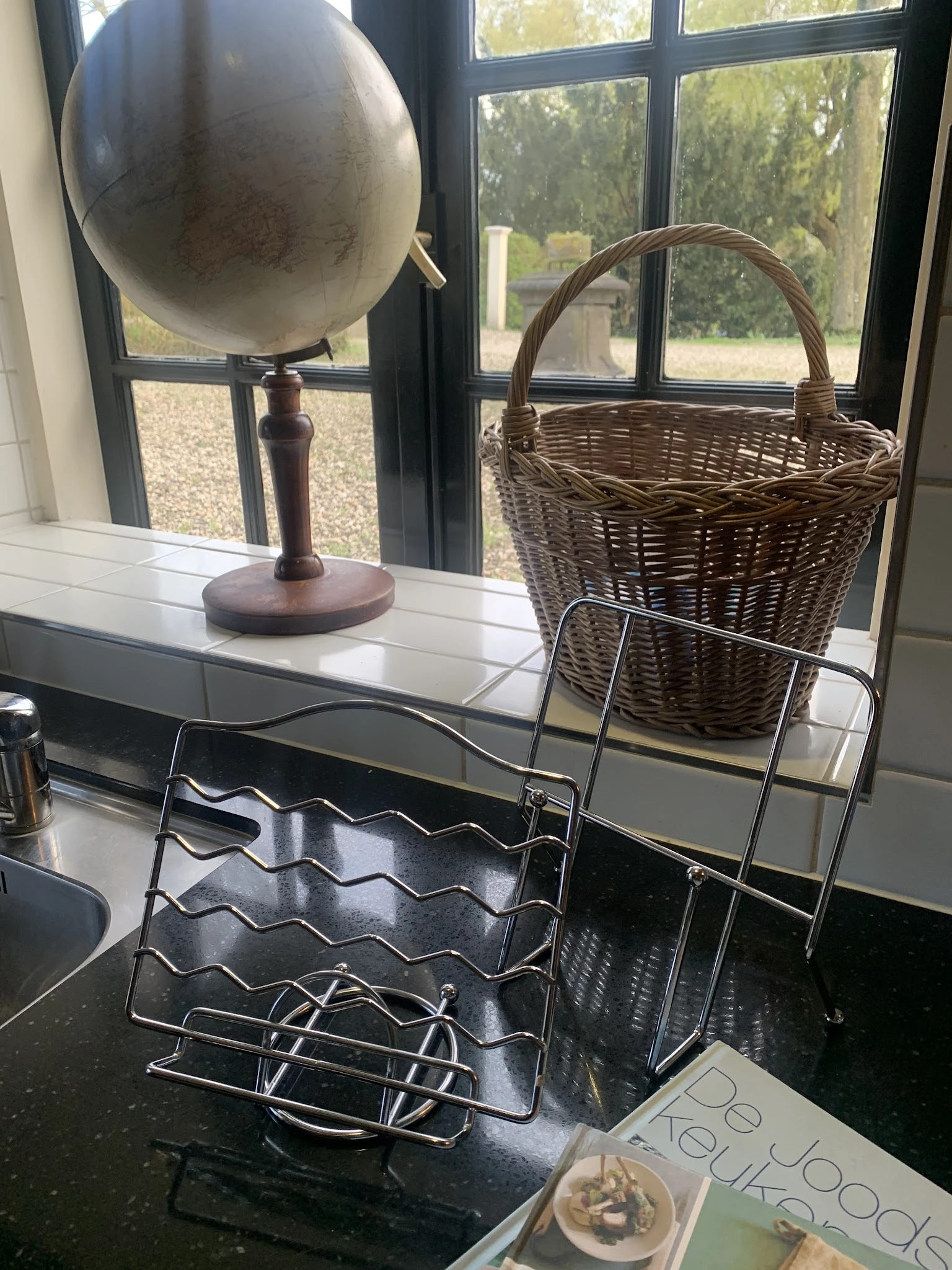 Verschillende huishoudelijke items op een toonbank: een houten lamp, een metalen rekje en een wenen mand
