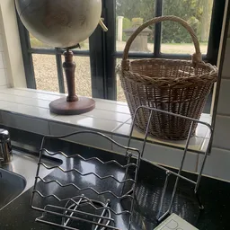 Verschillende huishoudelijke items op een toonbank: een houten lamp, een metalen rekje en een wenen mand