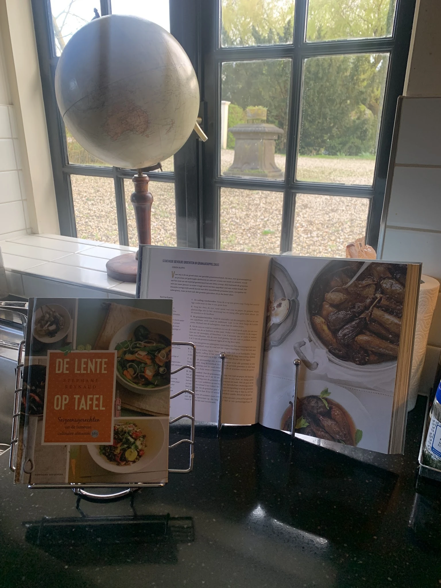 Stapel kookboeken en receptenboeken op een tafel bij een raam