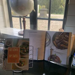 Stapel kookboeken en receptenboeken op een tafel bij een raam