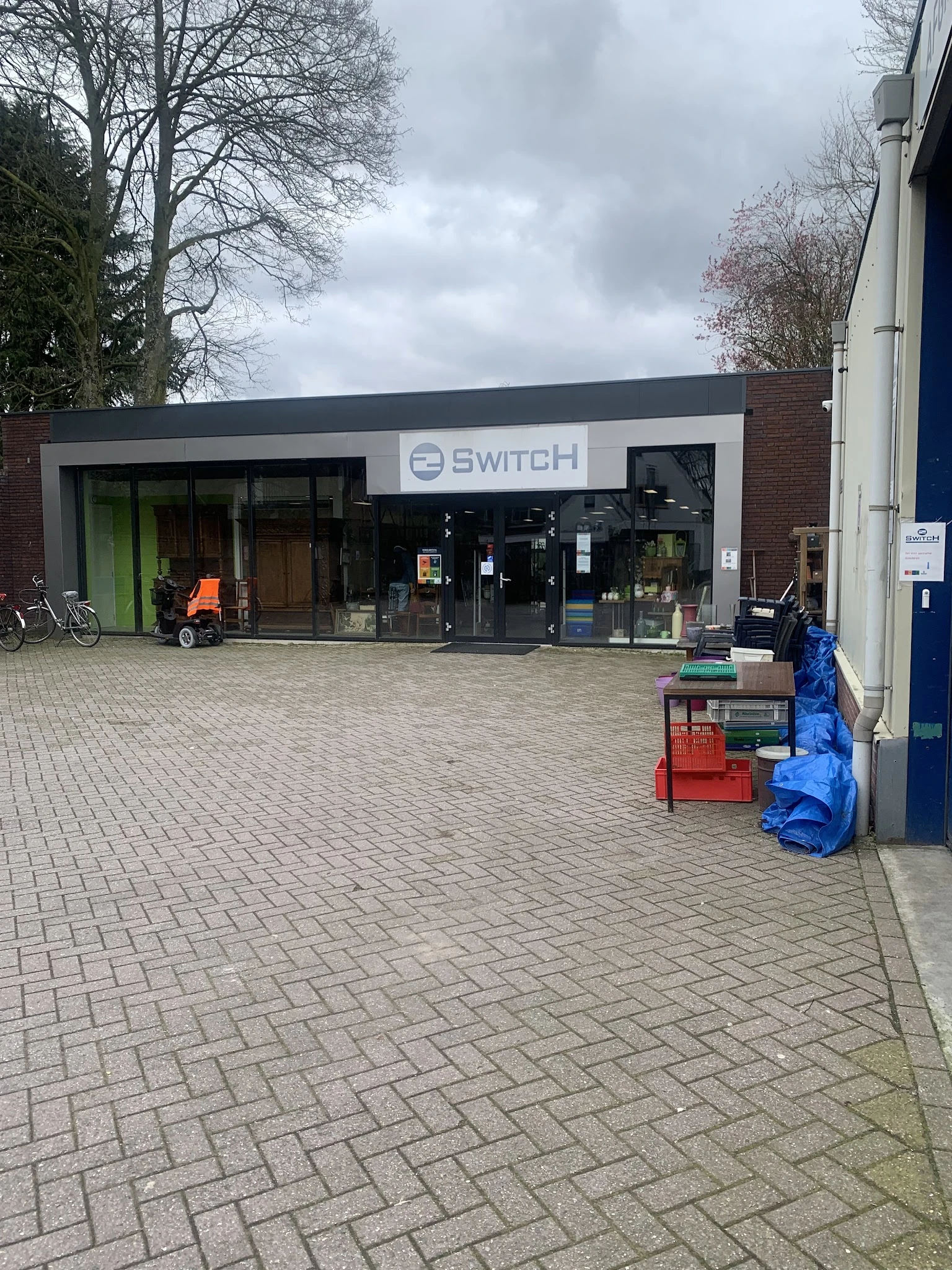 Voorgevel van kringloopwinkel 2Switch met groene en zwarte deuren, winkelnaam zichtbaar boven de ingang