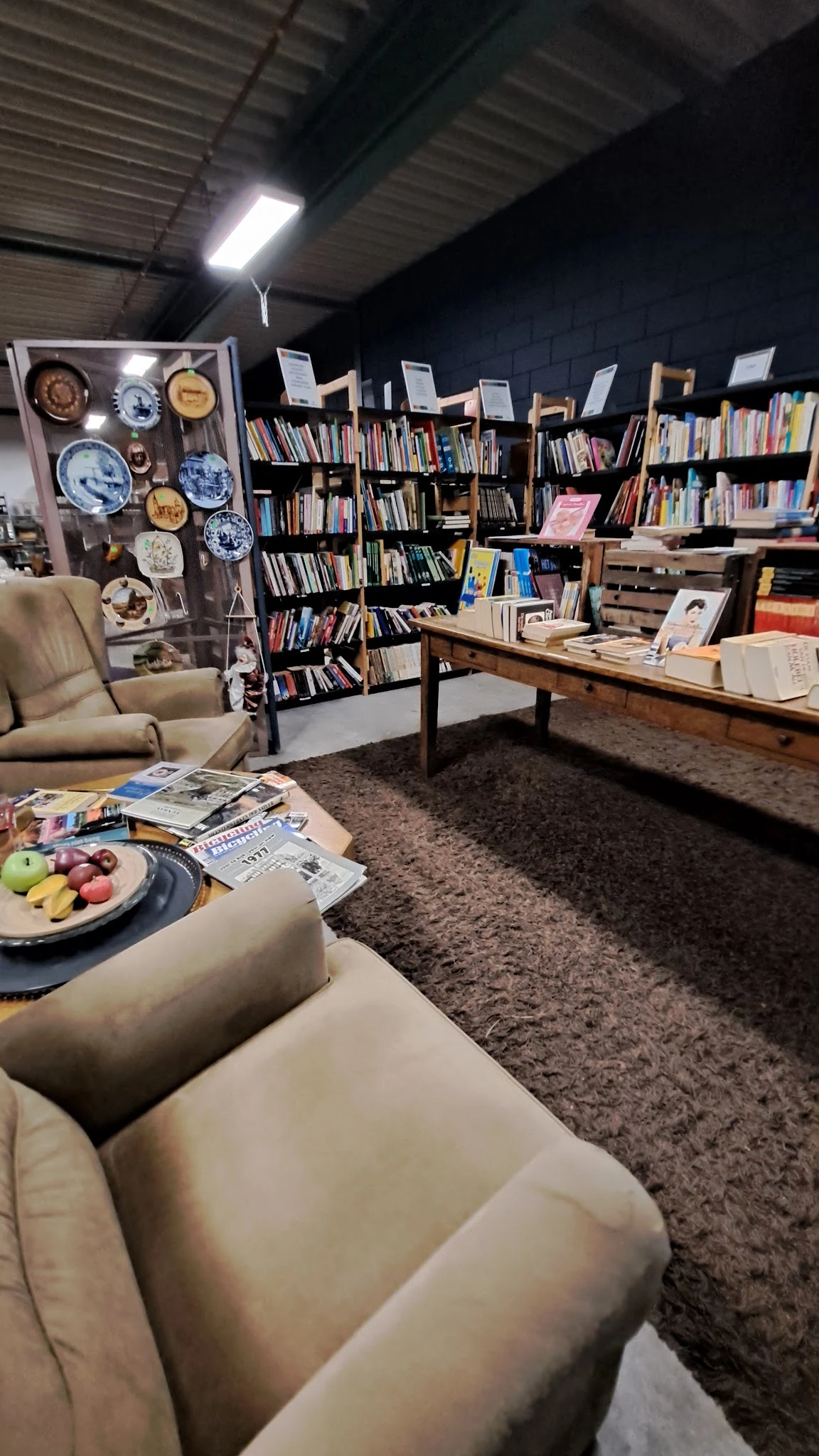 Gezellige leeshoek met fauteuil, lage tafel met fruitmand en tijdschriften, boekenrekken op de achtergrond