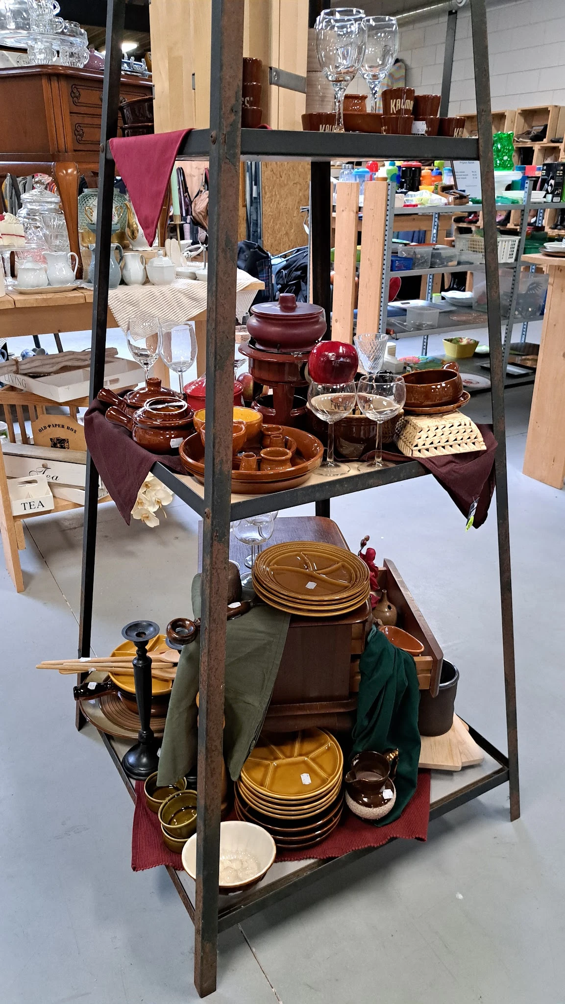Uitstalling van tweedehands aardewerk, servies en theepotten in bruin- en roodtinten op schappen