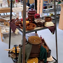 Uitstalling van tweedehands aardewerk, servies en theepotten in bruin- en roodtinten op schappen
