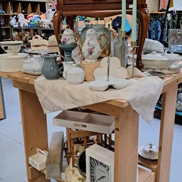 Houten tafel met wit serviesgoed, kandelaars en decoratieve items uitgestald in een kringloopwinkel