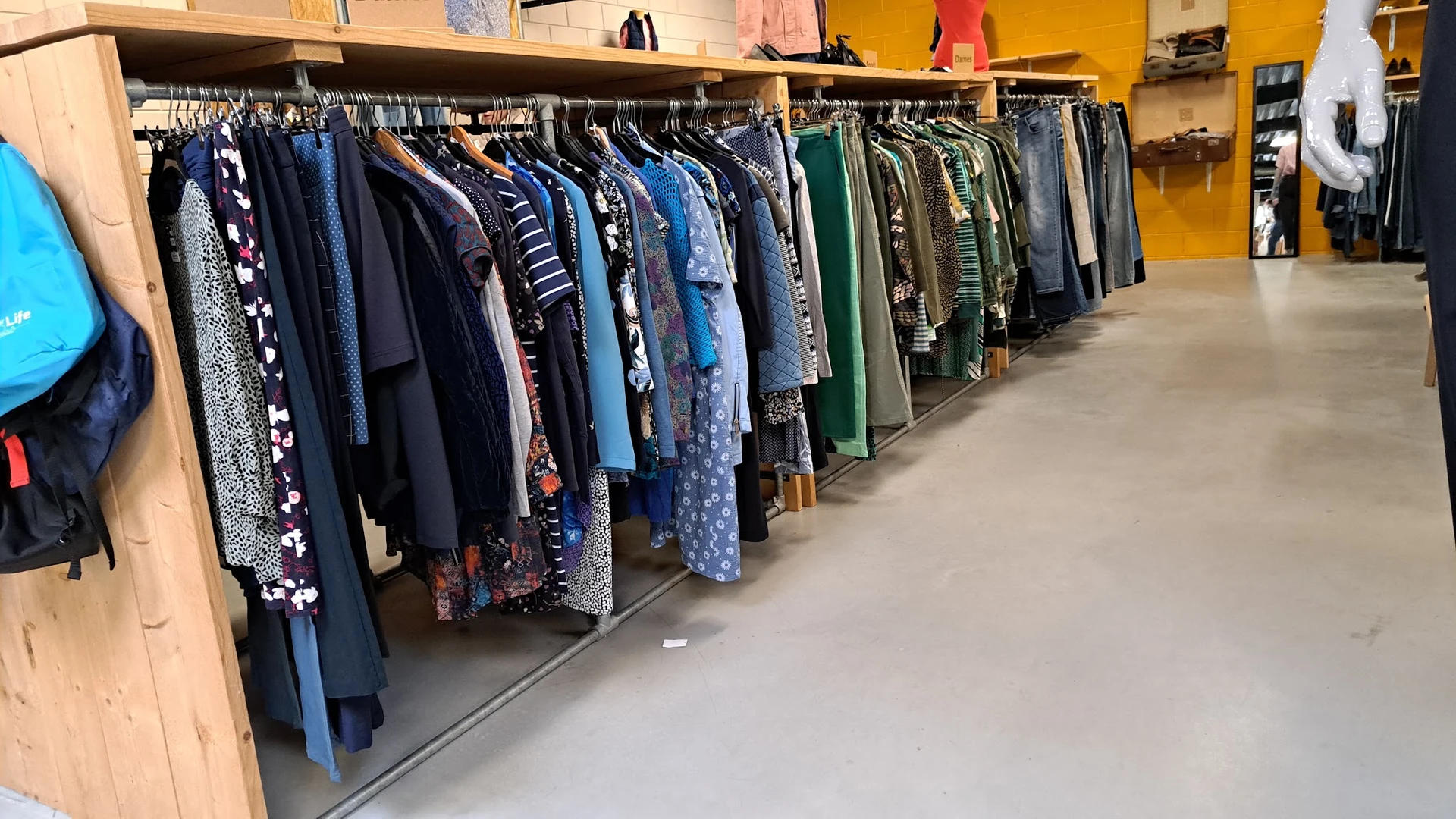Lange rekken met tweedehands kleding in verschillende kleuren, voornamelijk blauwtinten en groene tinten