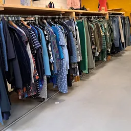Lange rekken met tweedehands kleding in verschillende kleuren, voornamelijk blauwtinten en groene tinten