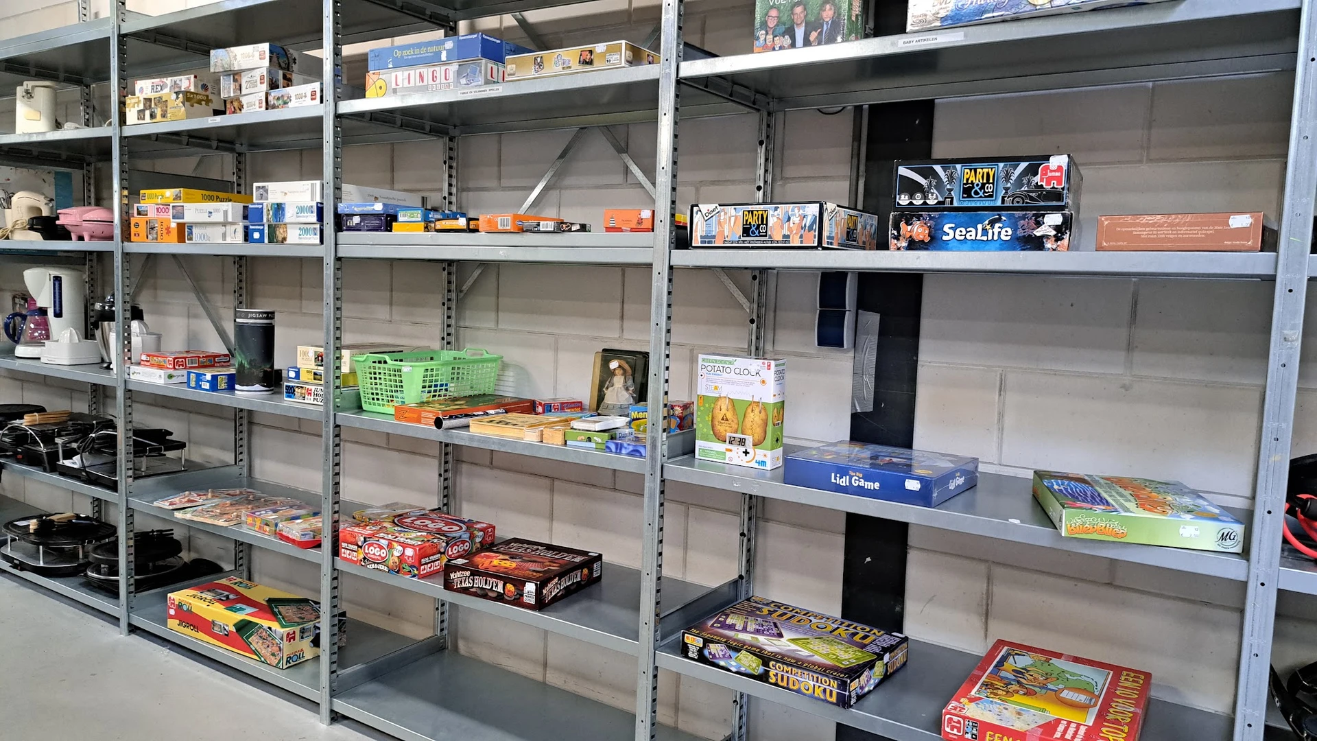 Metalen stellingen met diverse tweedehands artikelen zoals bordspellen, boeken en huishoudartikelen