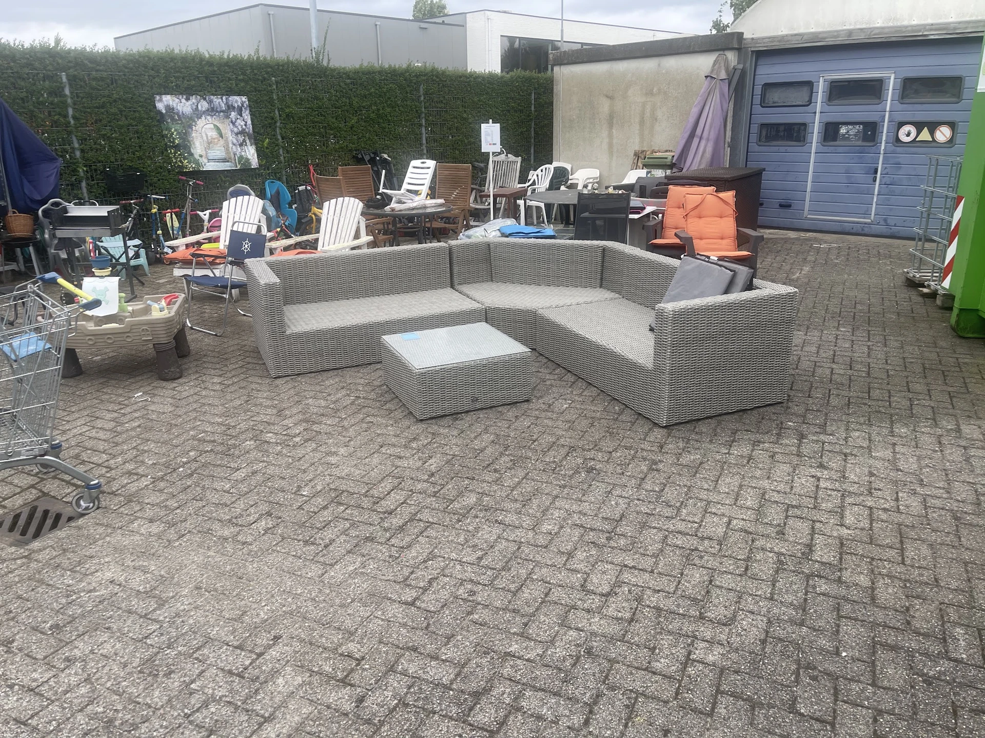 Grijze rotan loungezetel met bijzettafel op een terras achter de winkel