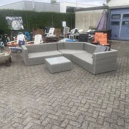Grijze rotan loungezetel met bijzettafel op een terras achter de winkel