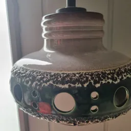 Close-up van een zwarte decoratieve trommel of vaas met gaten en patroon, onder een lamp