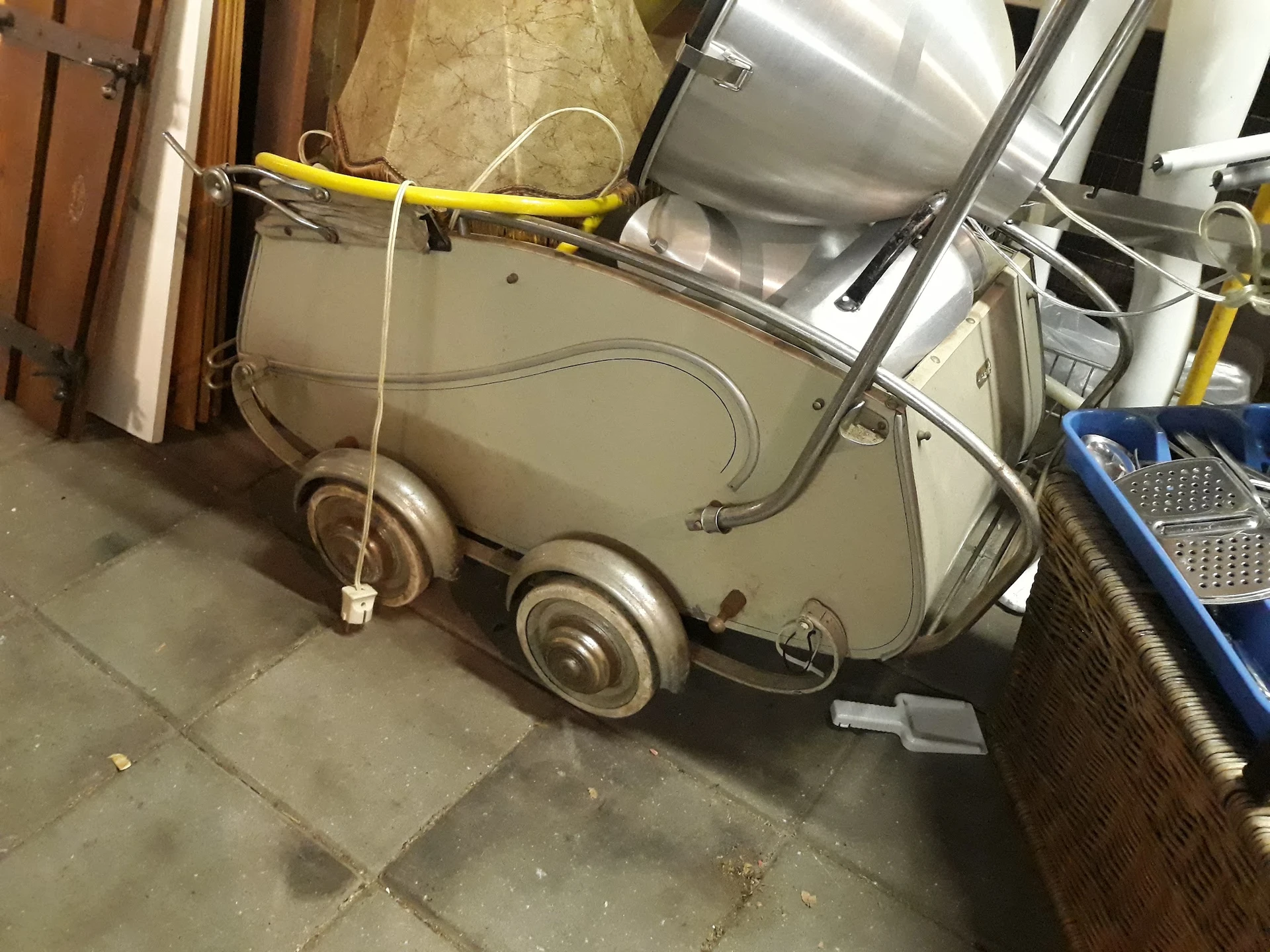 Vintage kinderwagen in beige/crème kleur op wielen in een opslagruimte
