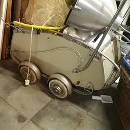 Vintage kinderwagen in beige/crème kleur op wielen in een opslagruimte