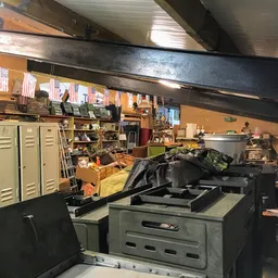 Zolder met stellingen, kasten, diverse spullen en een grote zwarte printer of apparaat op een tafel