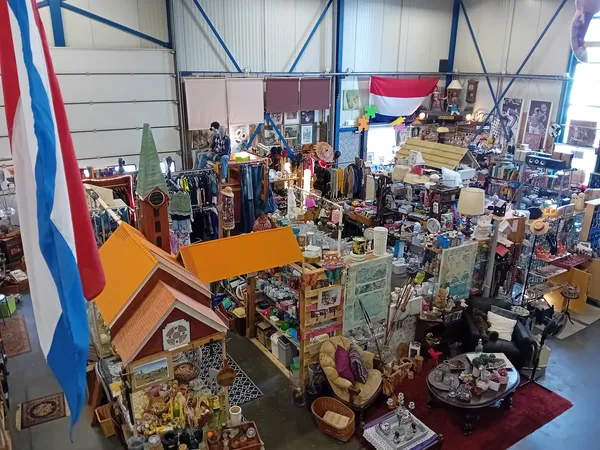 Overzicht van kringloopwinkel met diverse spullen, kleding, meubels en decoratie uitgestald op vloer en stellingen, Nederland
