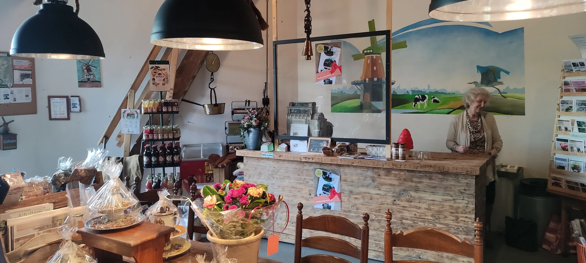 Binnenaanzicht van een lunchroom met houten toonbank, zwarte hanglamp, bloemen, koffieapparatuur en menukaarten