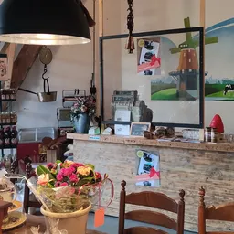 Binnenaanzicht van een lunchroom met houten toonbank, zwarte hanglamp, bloemen, koffieapparatuur en menukaarten