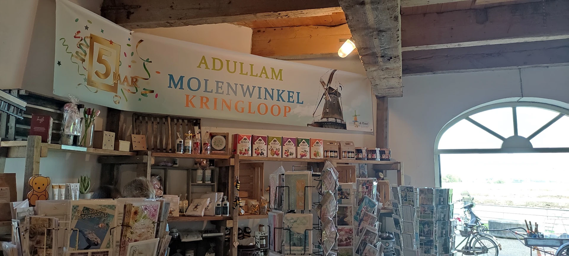 Winkelinterieur met stellingen vol spullen, winkelnaambord met molen aan plafond