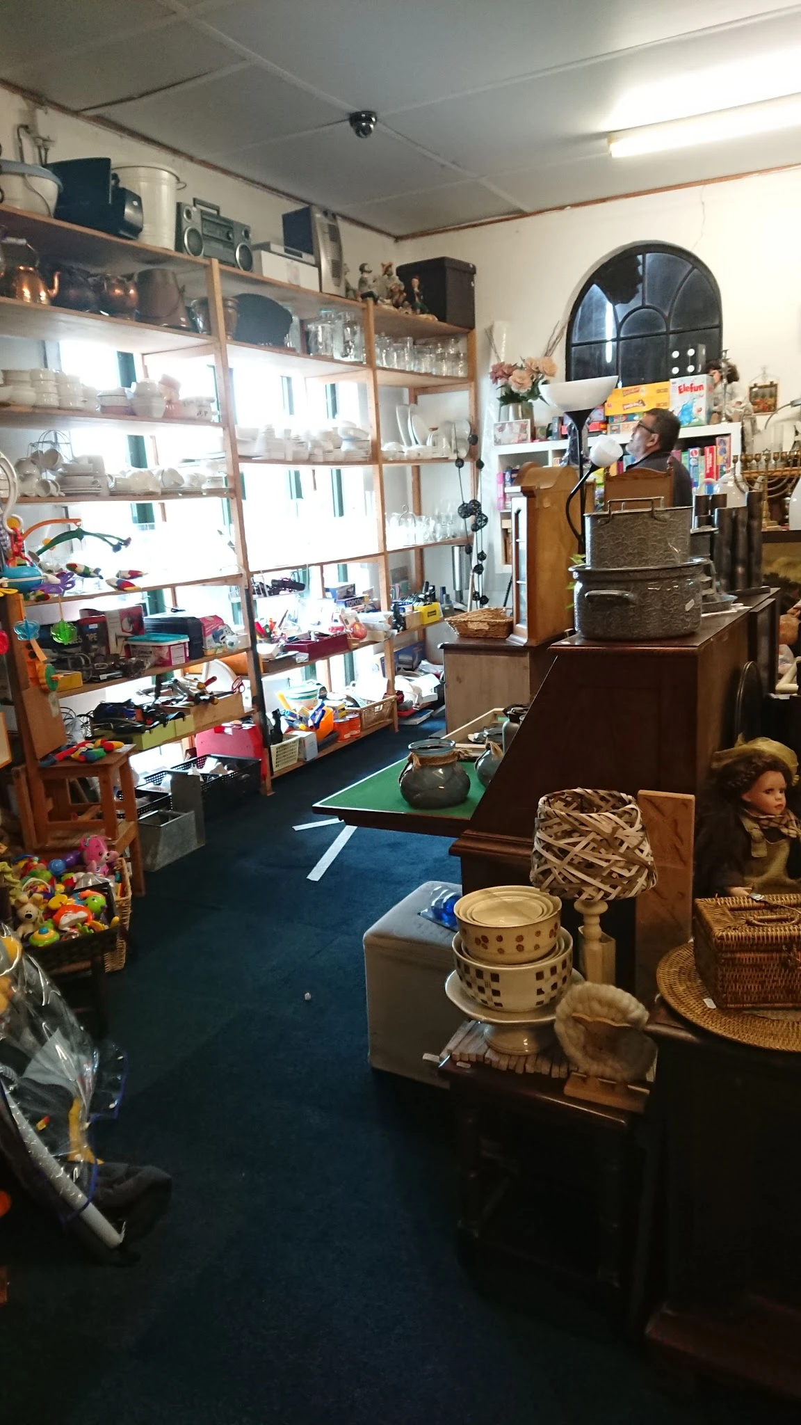 Binnenaanzicht van kringloopwinkel met diverse spullen, meubels en artikelen verspreid over de vloer en in stellingen