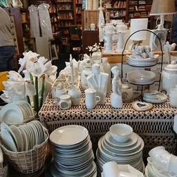 Uitstalling van wit servies, kandelaars en decoratieve items op tafel met patroonkleed