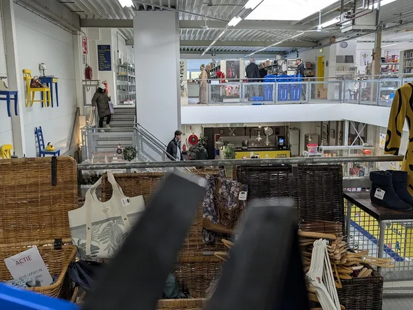 Winkelinterieur met mezzanine, stellingen met spullen en bezoekers op de begane grond