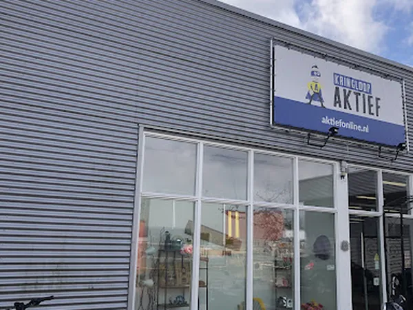 Voorgevel van kringloopwinkel Aktief met grijze golfplaten wand, grote ramen en blauwe winkelnaambord