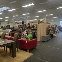Winkelvloer met rode zitmeubels, tafels, stellingen met spullen en dividers in een kringloopwinkel