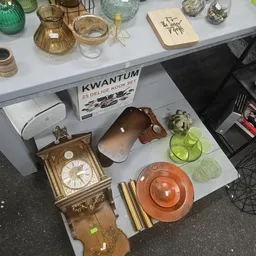 Uitgestalde tweedehands huishoudartikelen: klok, servies, glazen, decoratie en keukengerei op display