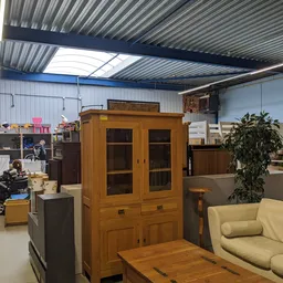 Winkelvloer met houten meubels, groene bank en diverse tweedehands artikelen onder golfplaten plafond