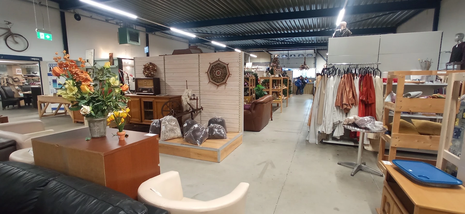 Winkelvloer van kringloopwinkel met meubels, kleding aan rekken, en diversen huishoudelijke spullen