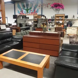 Winkelvloer met zwarte leren zithoeken, houten salontafel en houten dressoirs op de achtergrond