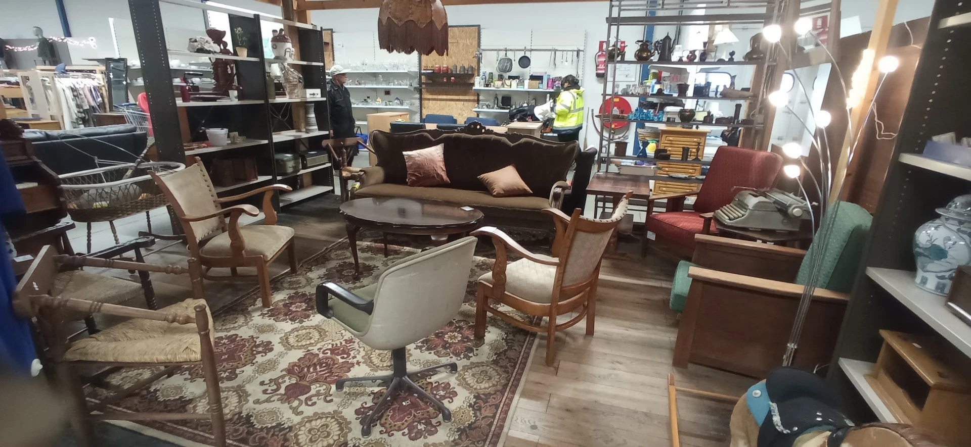 Winkelvloer met bruine bank, houten stoelen, salontafel en boekenkasten met diversen spullen