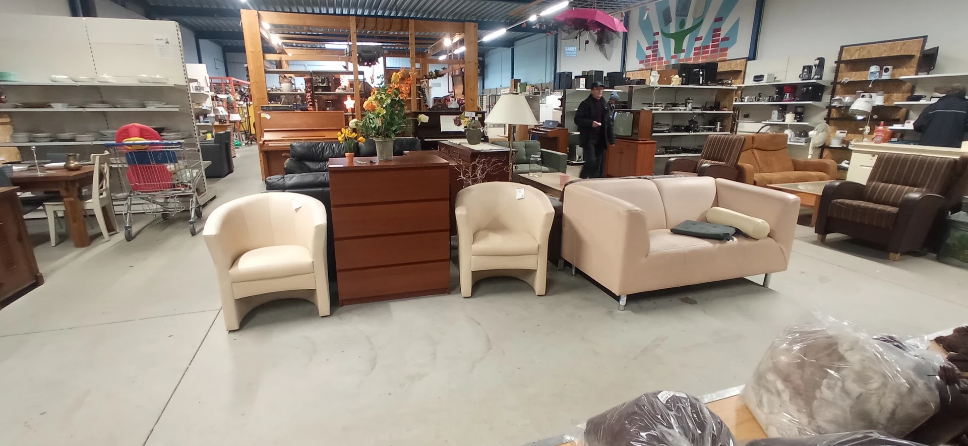 Beige en crème gekleurde fauteuils en een bank uitgestald in de winkel, met een bruin dressoir ertussen