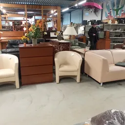 Beige en crème gekleurde fauteuils en een bank uitgestald in de winkel, met een bruin dressoir ertussen
