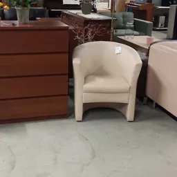 Uitgestalde fauteuils en dressoir in een kringloopwinkel, waaronder een beige en roze stoelen en een bruine houten kast