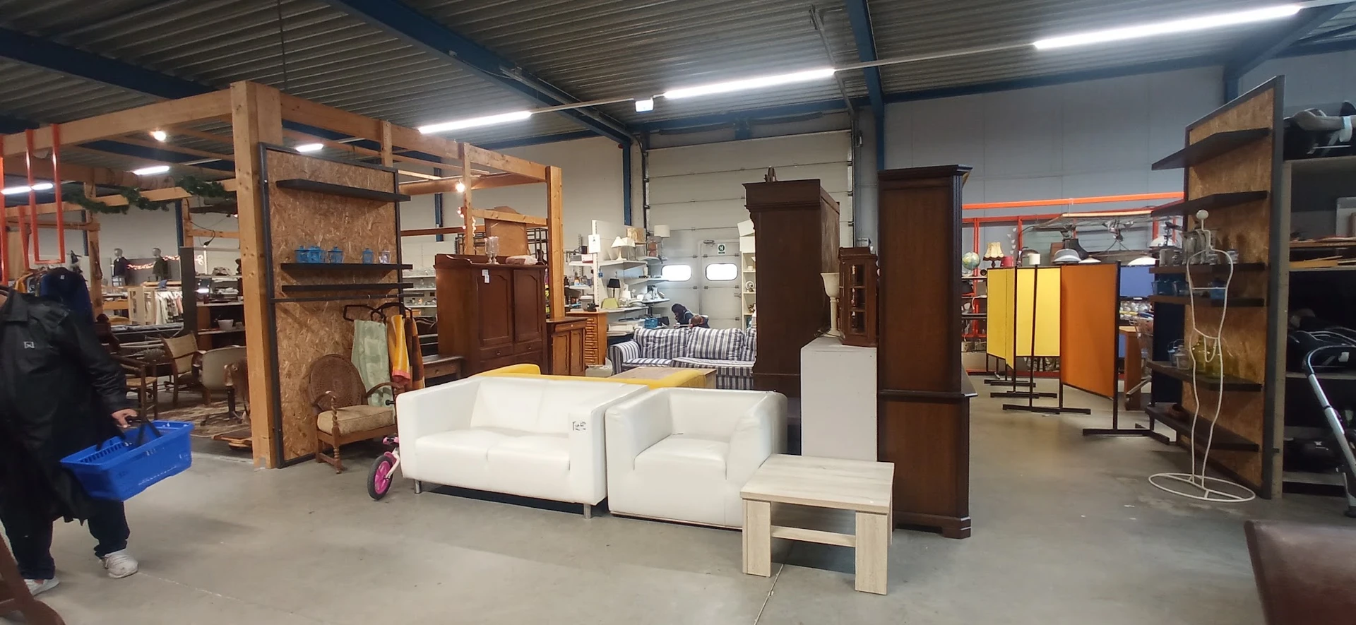 Witte zithoek met bank en fauteuils naast houten kasten en meubels in kringloopwinkel